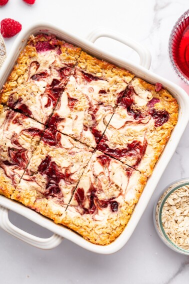 Cottage cheese baked oatmeal in a white baking dish showing creamy cottage cheese and raspberry jam swirls on top.