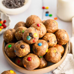 Monster cookie protein balls stacked in a bowl with colorful M&M’s and mini chocolate chips.