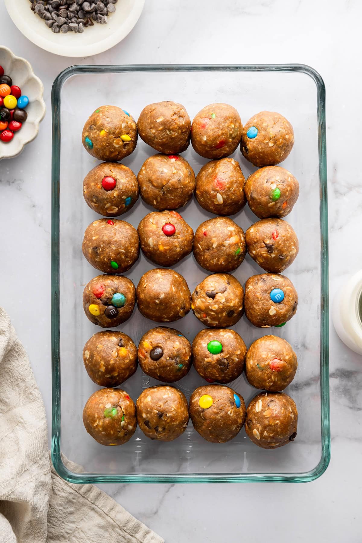 no bake cookie protein balls Finished monster cookie protein balls lined up in a glass container for fridge storage.