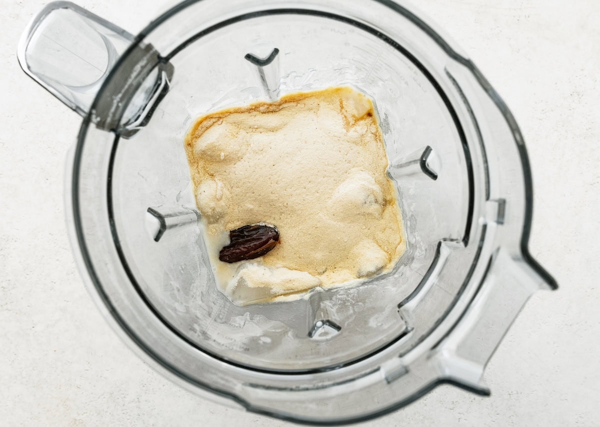 Blender filled with shake ingredients including ice, almond butter and a medjool date before blending.