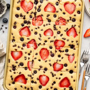 Sheet pan pancakes topped with strawberries and chocolate chips, freshly baked and cut into squares.