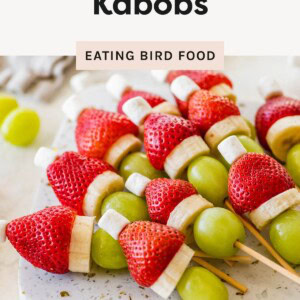 Grinch fruit kabobs made with strawberries, banana slices, green grapes, and mini marshmallows arranged on a serving board for a festive holiday snack