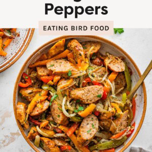 Bowl of sliced sausage with roasted bell peppers and onions, garnished with herbs.