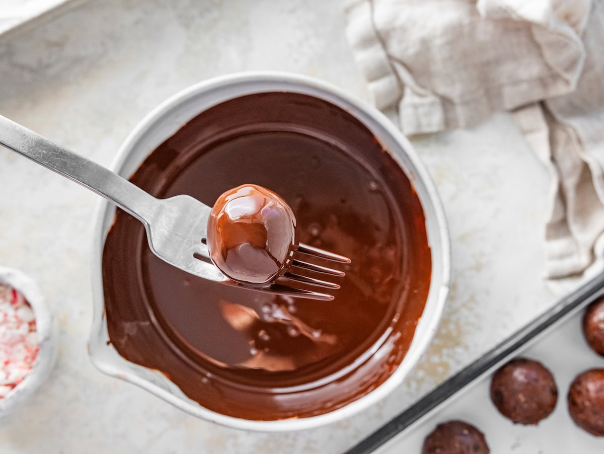 dipping a protein ball A fork dipping a protein ball into melted chocolate in a small bowl.