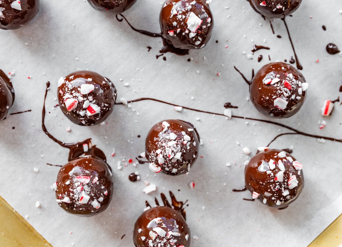 Chocolate peppermint protein balls recipe Chocolate peppermint protein balls drying on parchment coated in chocolate and topped with crushed candy canes.