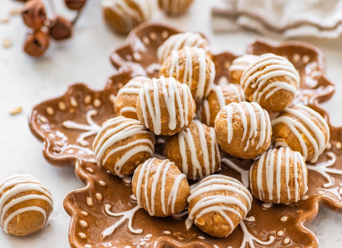 Gingerbread Protein Balls Plate of gingerbread protein balls with white chocolate drizzle arranged on a festive snowflake plate.