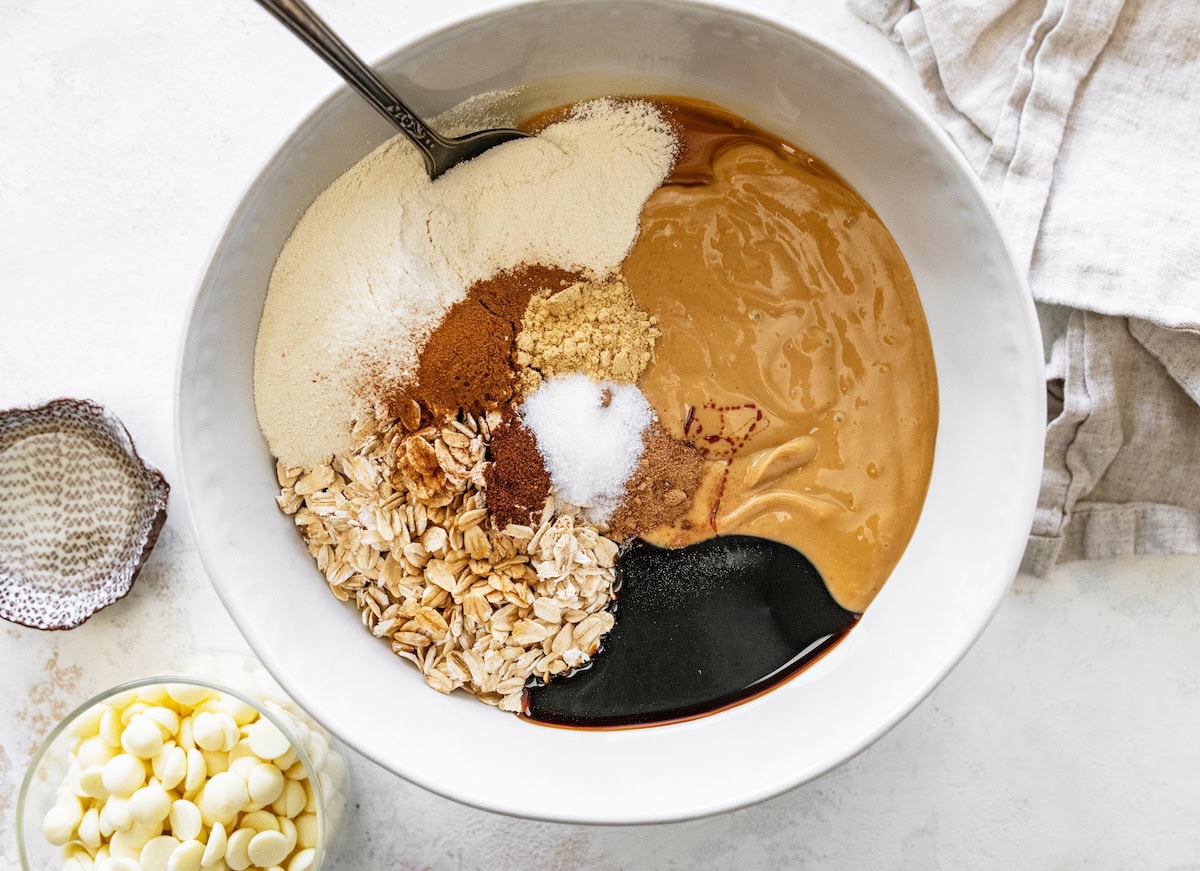 ingredients in bowl Mixing bowl filled with oats, spices, molasses, protein powder and cashew butter before stirring.
