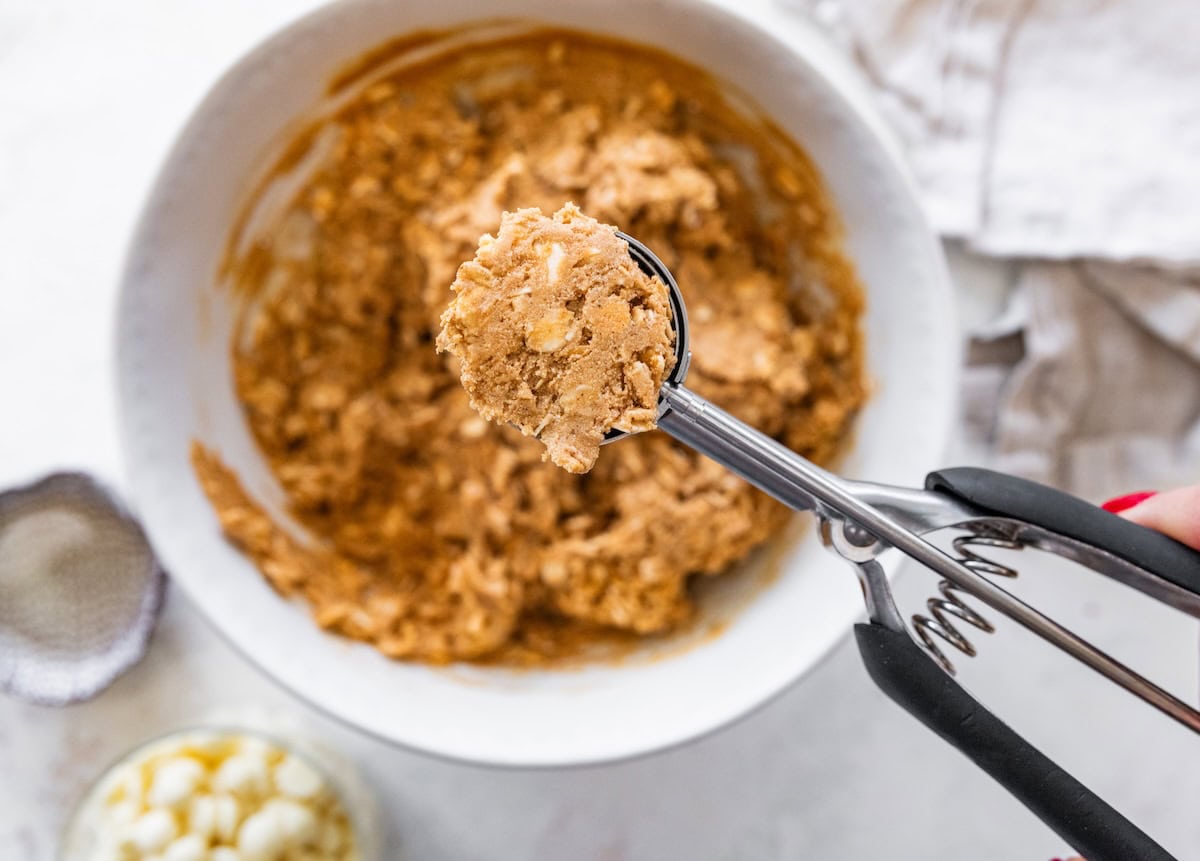 gingerbread protein ball scoop Cookie scoop lifting gingerbread protein ball mixture from a mixing bowl before rolling into balls.