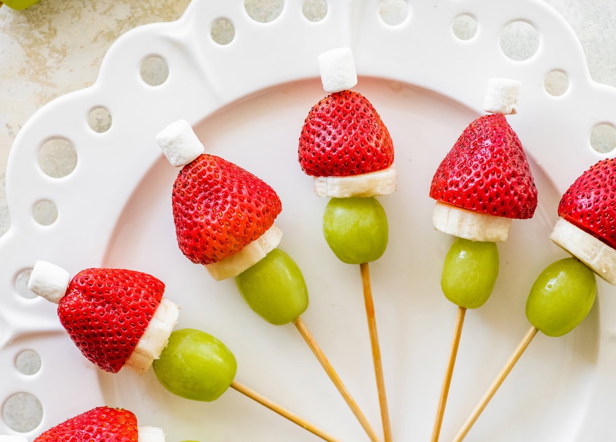Close-up of assembled Grinch fruit kabobs lined up on a decorative white plate.
