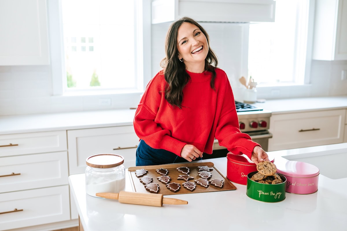 gingerbread cookies Brittany in a red sweater smiling in the kitchen with a tray of gingerbread cookies in front of her.