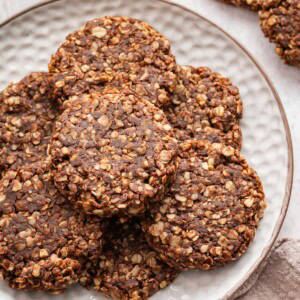 Multiple chocolate no bake cookies stacked on one another on a white plate.