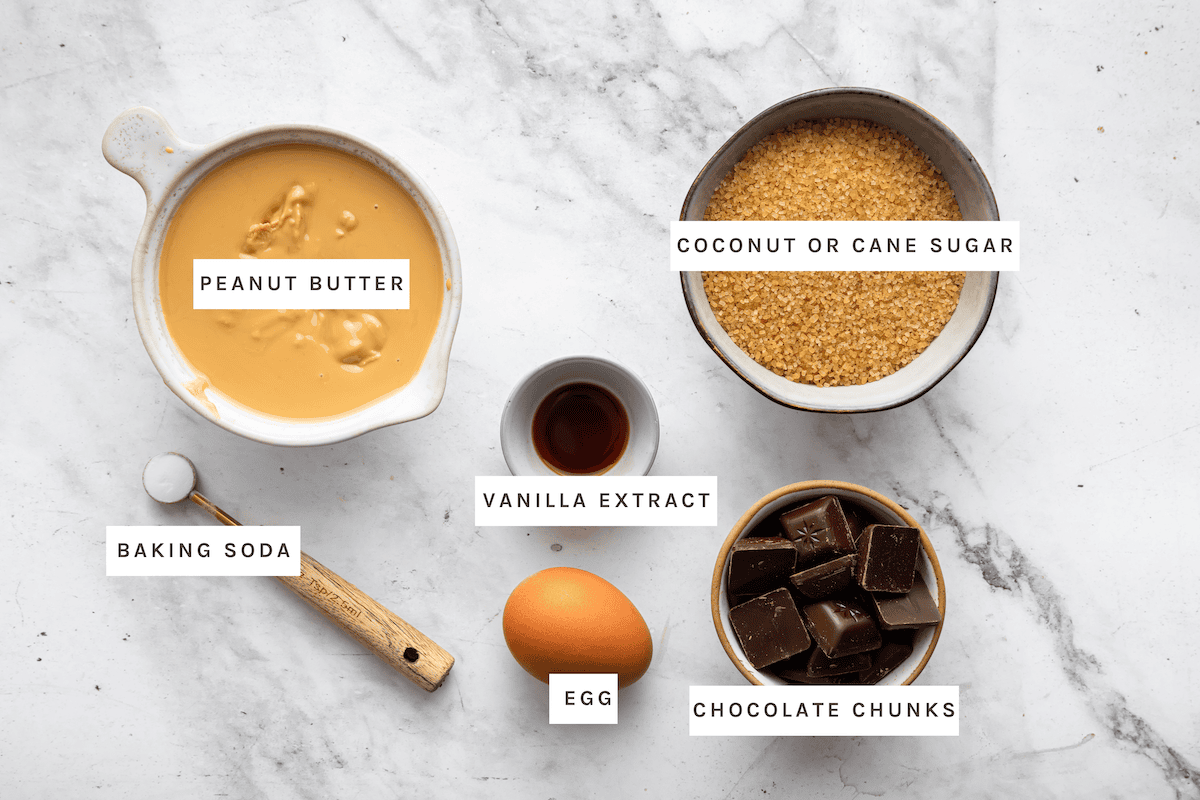 Ingredients measured for peanut butter blossoms: coconut sugar, peanut butter, baking soda, vanilla extract, an egg, and chocolate chunks.