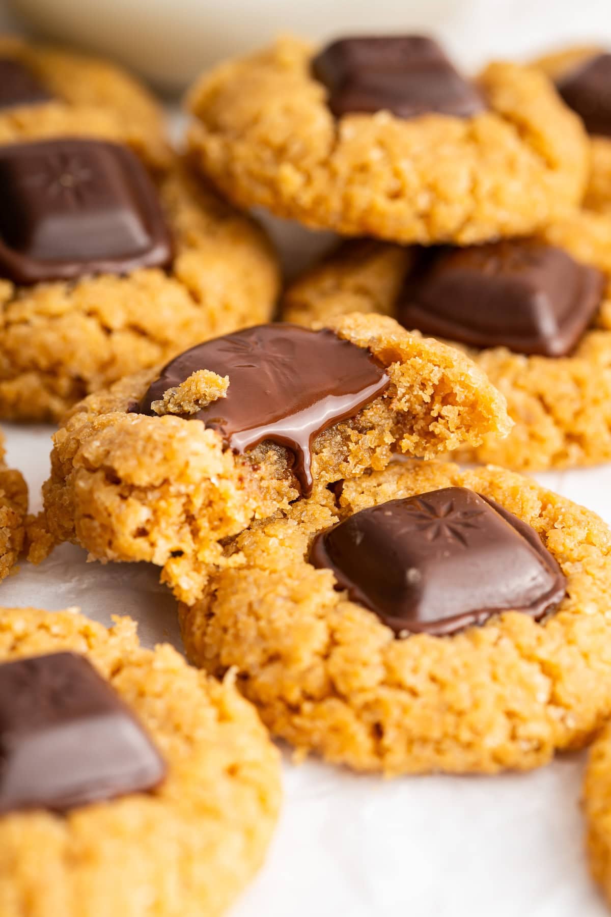 A peanut butter blossom cookie with a melting chocolate square in the middle and a bite taken out of the edge, surrounded by more cookies.