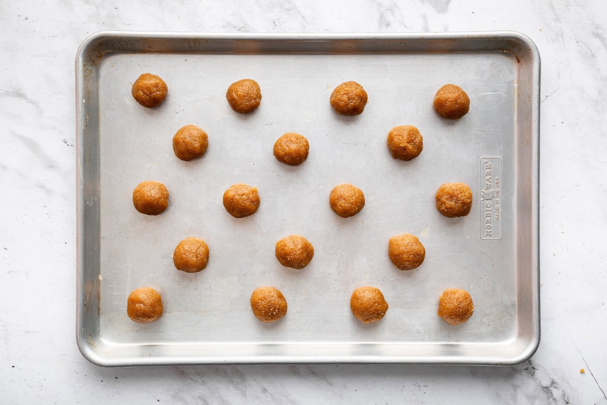 Rows of small peanut butter cookie dough balls arranged evenly on a metal baking sheet, ready to go into the oven.
