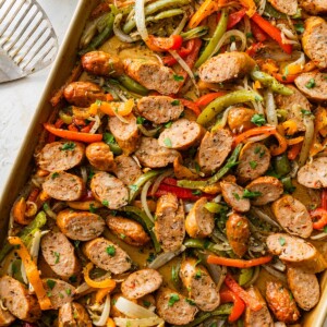 Close up sheet pan with sliced chicken sausage, roasted peppers and caramelized onions.