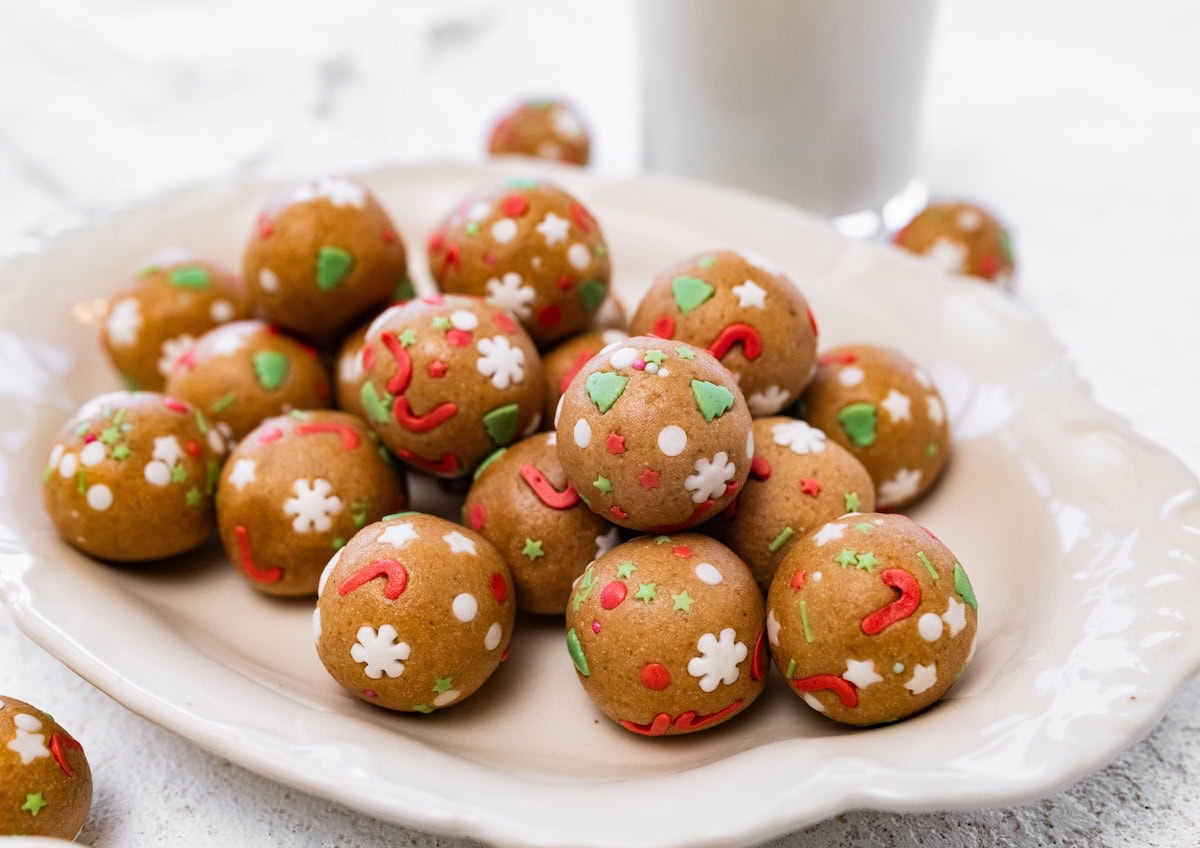Sugar Cookie Protein Balls A cream-colored plate piled with sugar cookie protein balls decorated with festive sprinkles.
