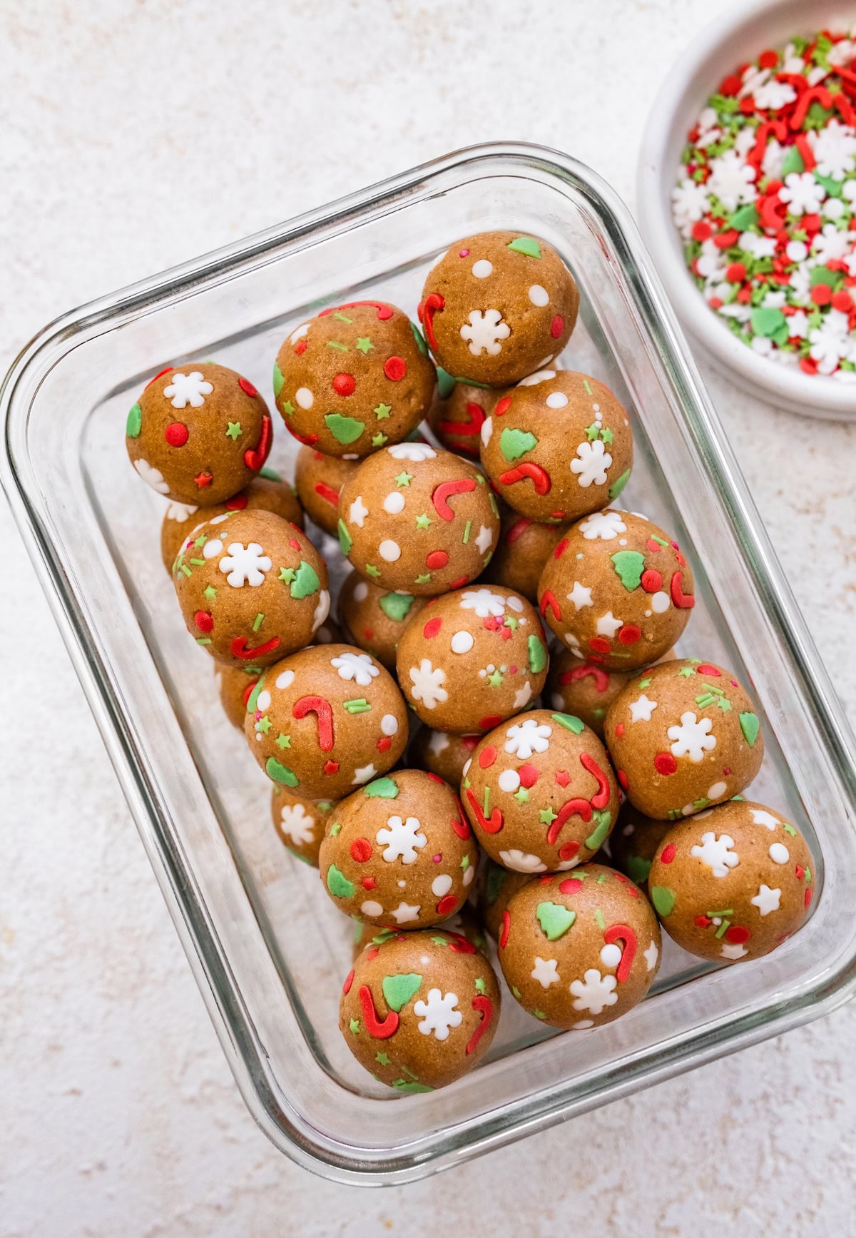 Sugar Cookie Protein Balls container A glass storage container filled with sugar cookie protein balls coated in red, green, and white holiday sprinkles.