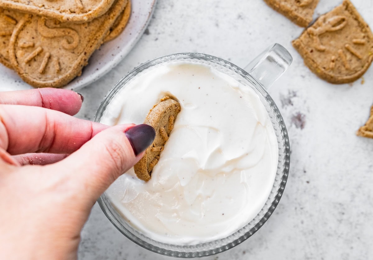 A woman's hand places a cookie inside a glass cup full of greek yogurt.