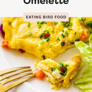 Close-up of a cottage cheese omelette with red bell peppers and chives, partially cut with a fork on a white plate.