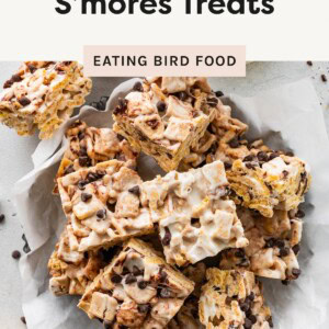 Stack of high-protein s’mores treats with melted marshmallows, graham cereal, and chocolate chips on parchment paper.