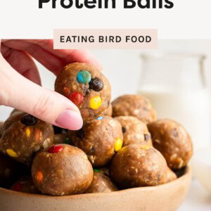 Hand picking up a monster cookie protein ball from a bowl of protein balls with colorful candy pieces.