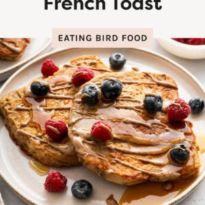 Two slices of protein French toast topped with blueberries and raspberries, drizzled with syrup and nut butter on a plate.
