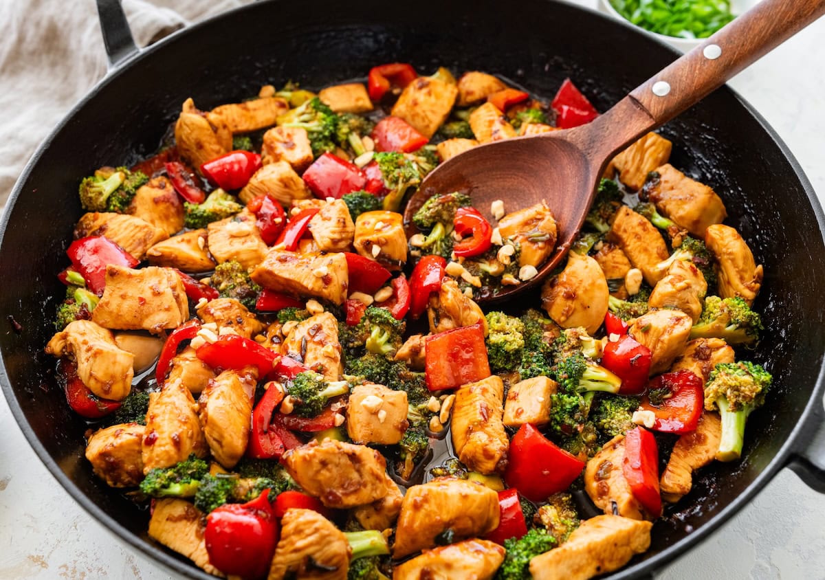 25-Minute Healthy Kung Pao Chicken Close-up of kung pao chicken with bell peppers and broccoli being stirred.