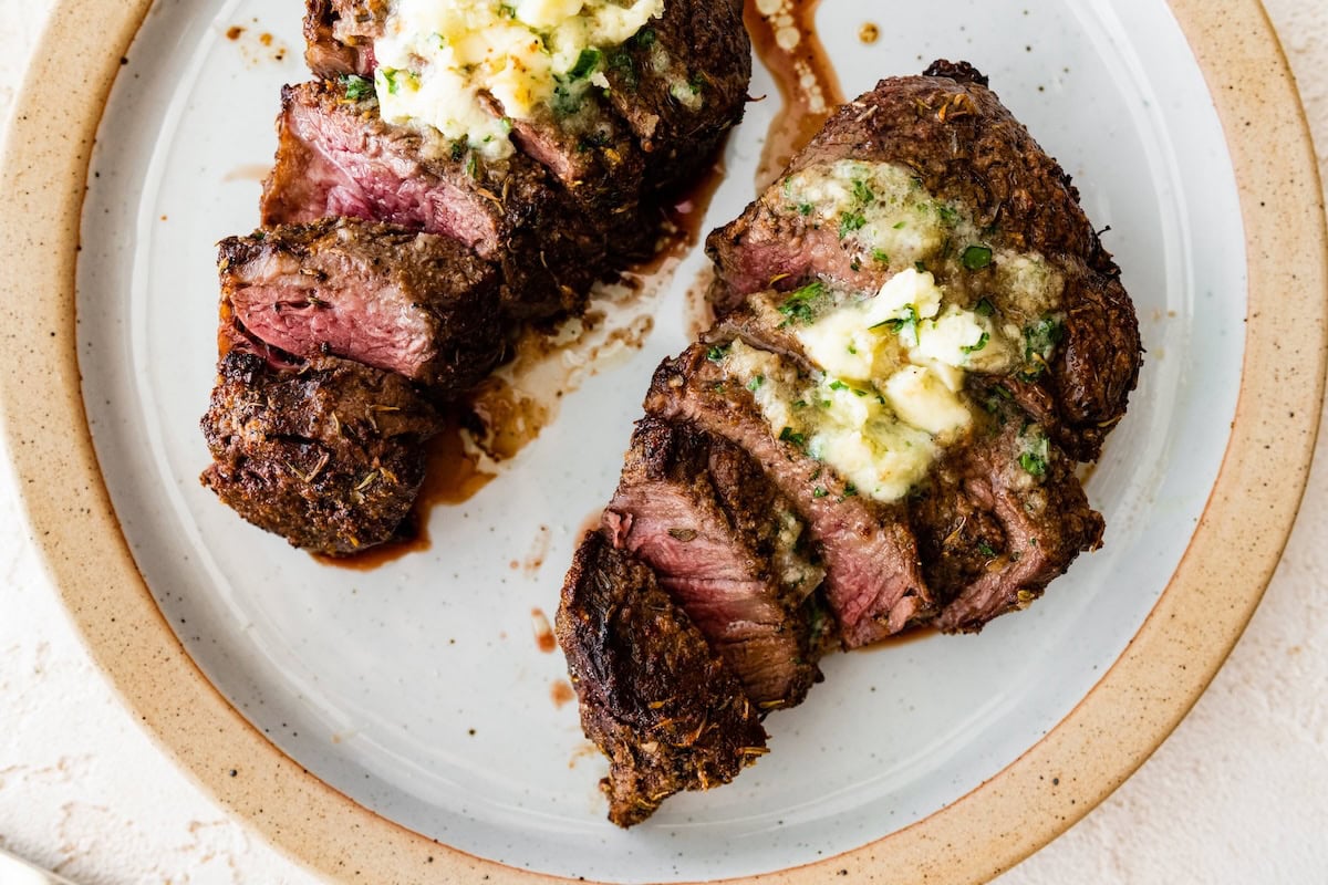 Two filet mignon pieces sliced on a white plate topped with garlic butter.