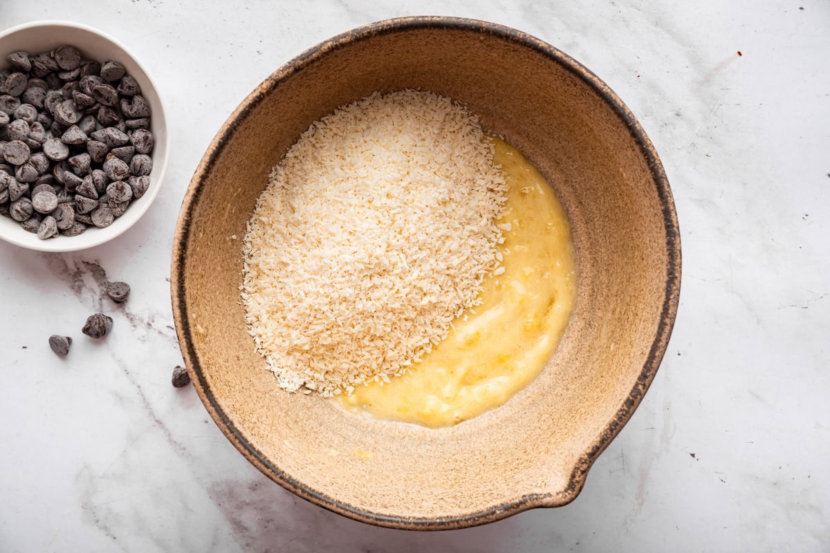Shredded coconut added to a large mixing bowl with mashed banana.