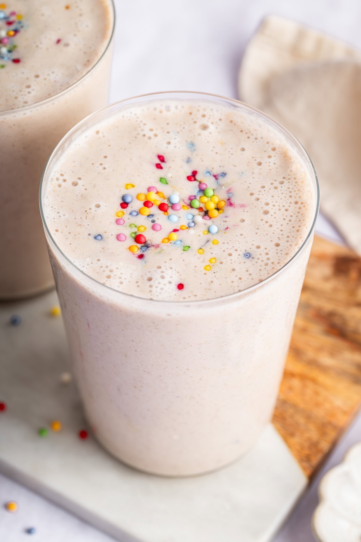 A cake batter protein shake in a glass topped with rainbow sprinkles.