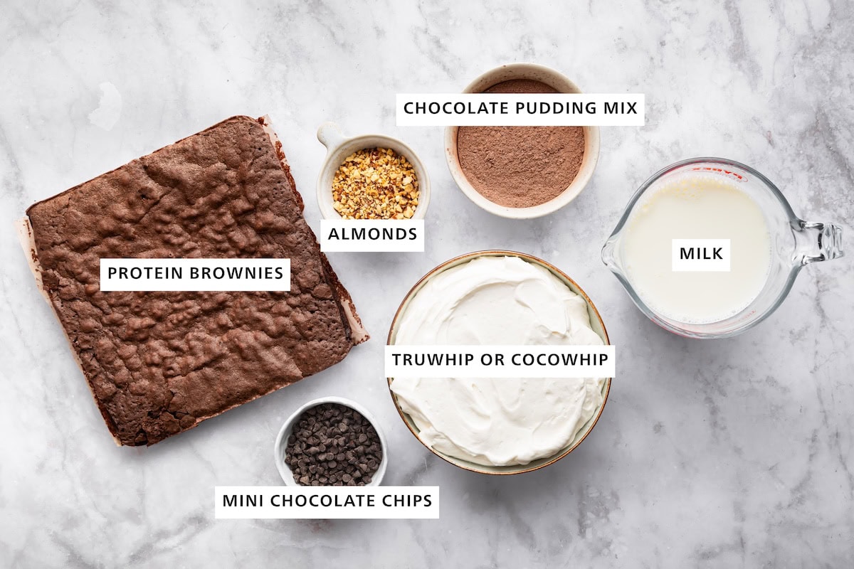 Ingredients used for a high-protein chocolate trifle includes: protein brownies, mini chocolate chips, truwhip, crushed almonds, chocolate pudding mix, and high-protein milk.