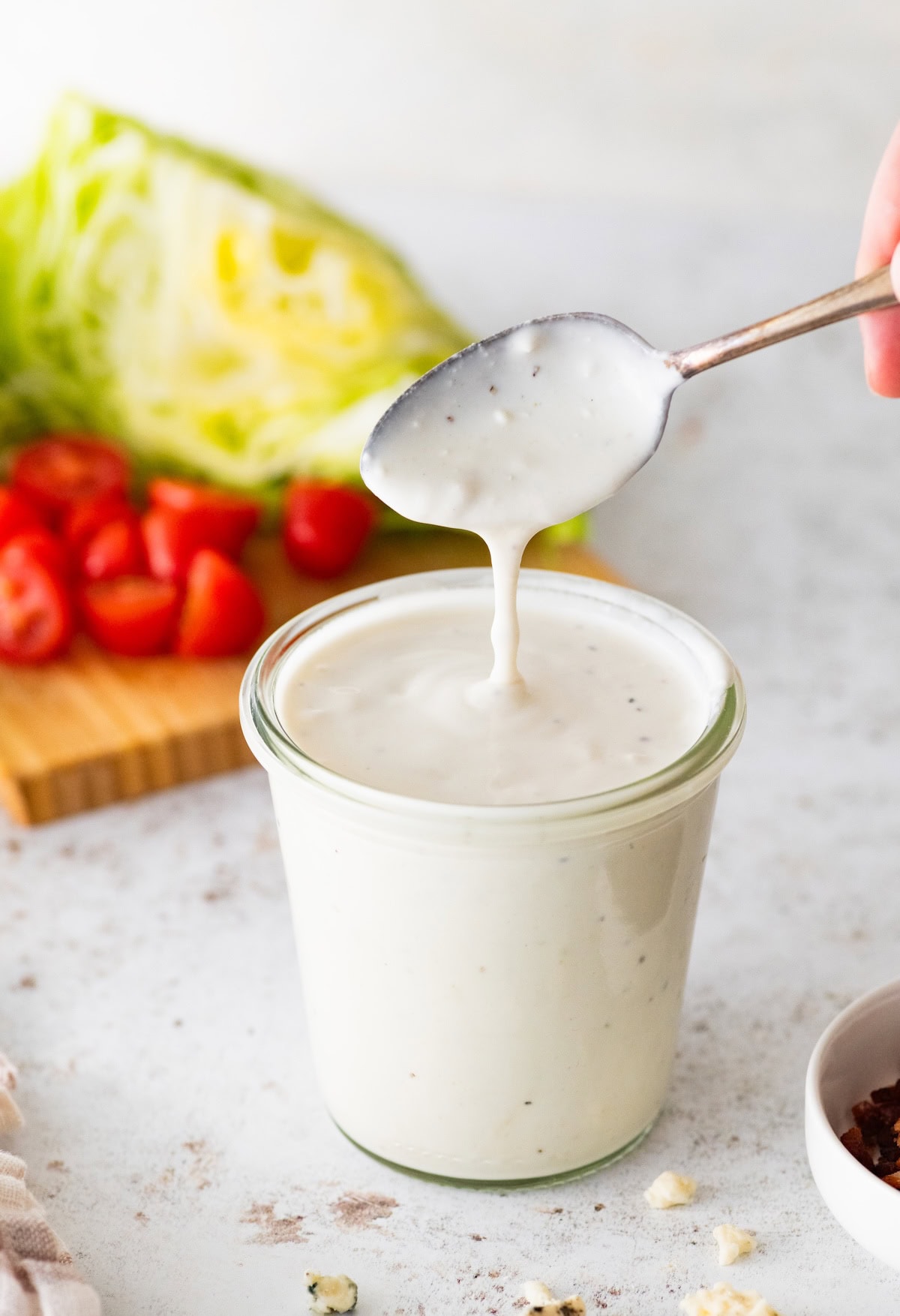 A spoon being lifted above a glass jar of Greek yogurt blue cheese dressing.