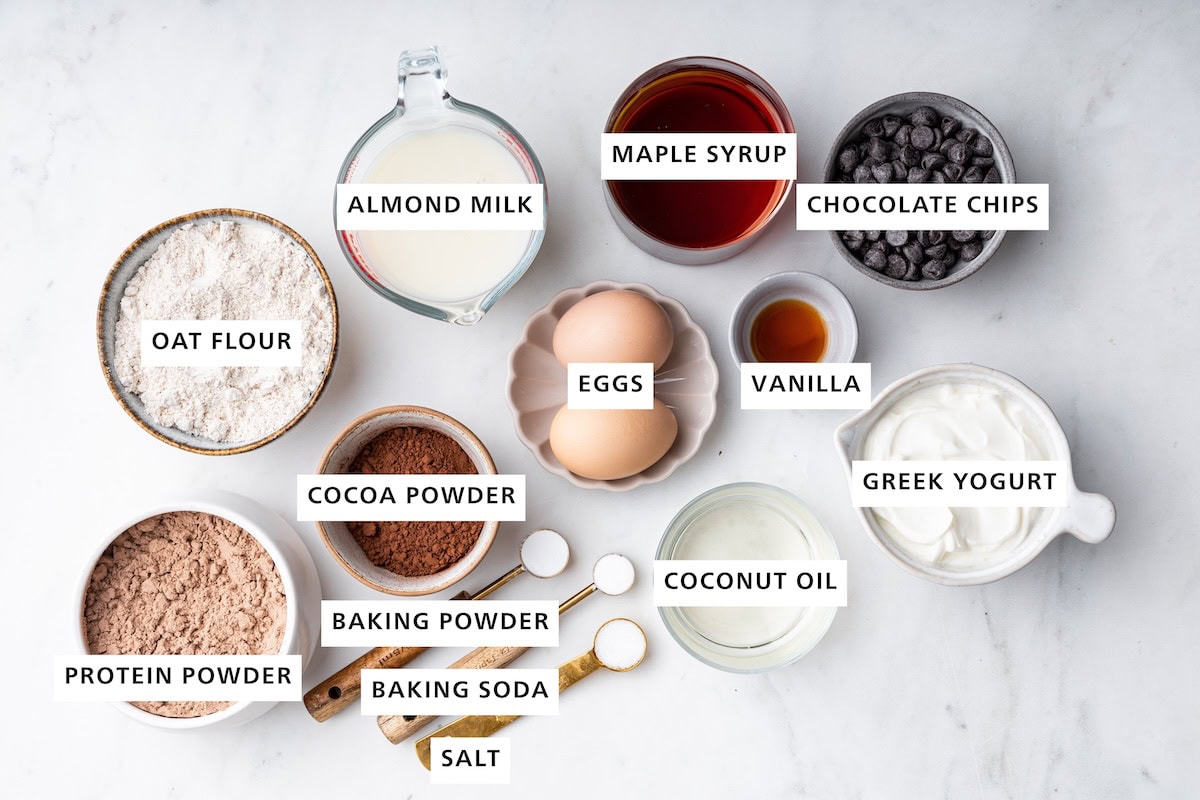 Ingredients measured out to make Protein Cake: vegan chocolate protein powder, oat flour, cocoa powder, almond milk, baking powder, baking soda, salt, eggs, maple syrup, coconut oil, vanilla, Greek yogurt and dark chocolate chips.