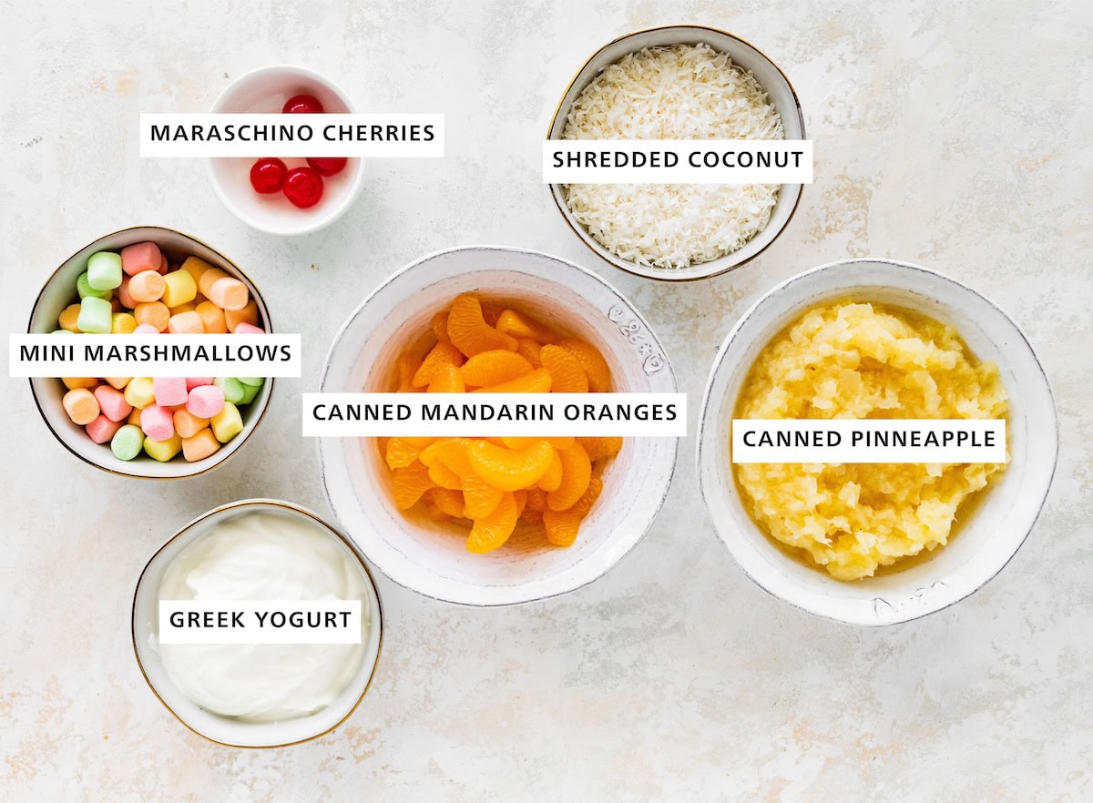 Ingredients measured out to make Healthy Ambrosia Salad: canned pineapple, shredded coconut, canned mandarin oranges, maraschino cherries, plain Greek yogurt and mini marshmallows.