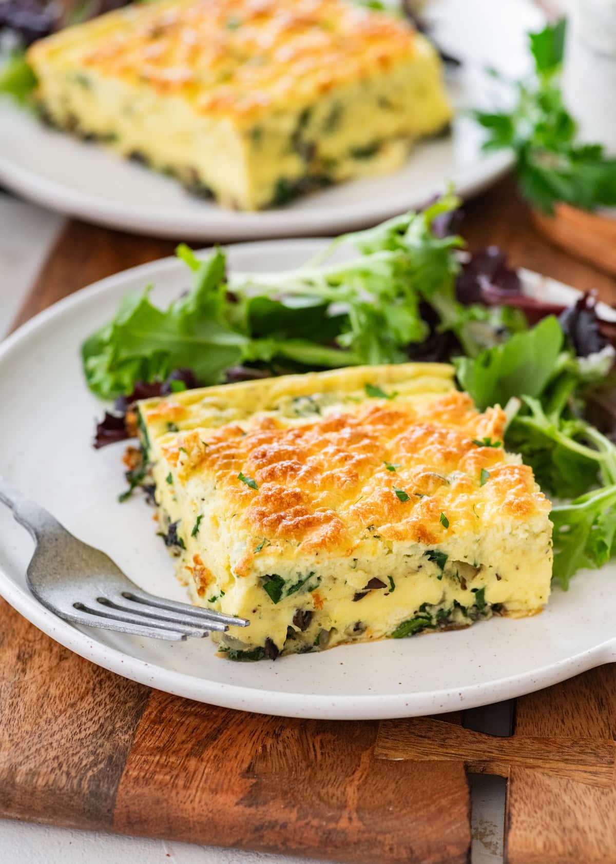 Slice of baked cottage cheese eggs with spinach served on plate with fresh greens.
