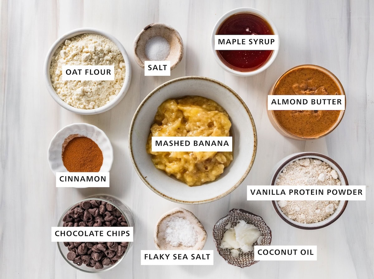 Ingredients for banana bread protein balls: mashed banana, oat flour, salt, maple syrup, almond butter, vanilla protein powder, coconut oil, sea salt, chocolate chips and cinnamon.