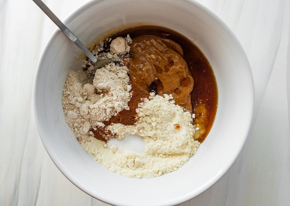 Ingredients for banana bread protein balls in a mixing bowl being mixed together with a spoon.