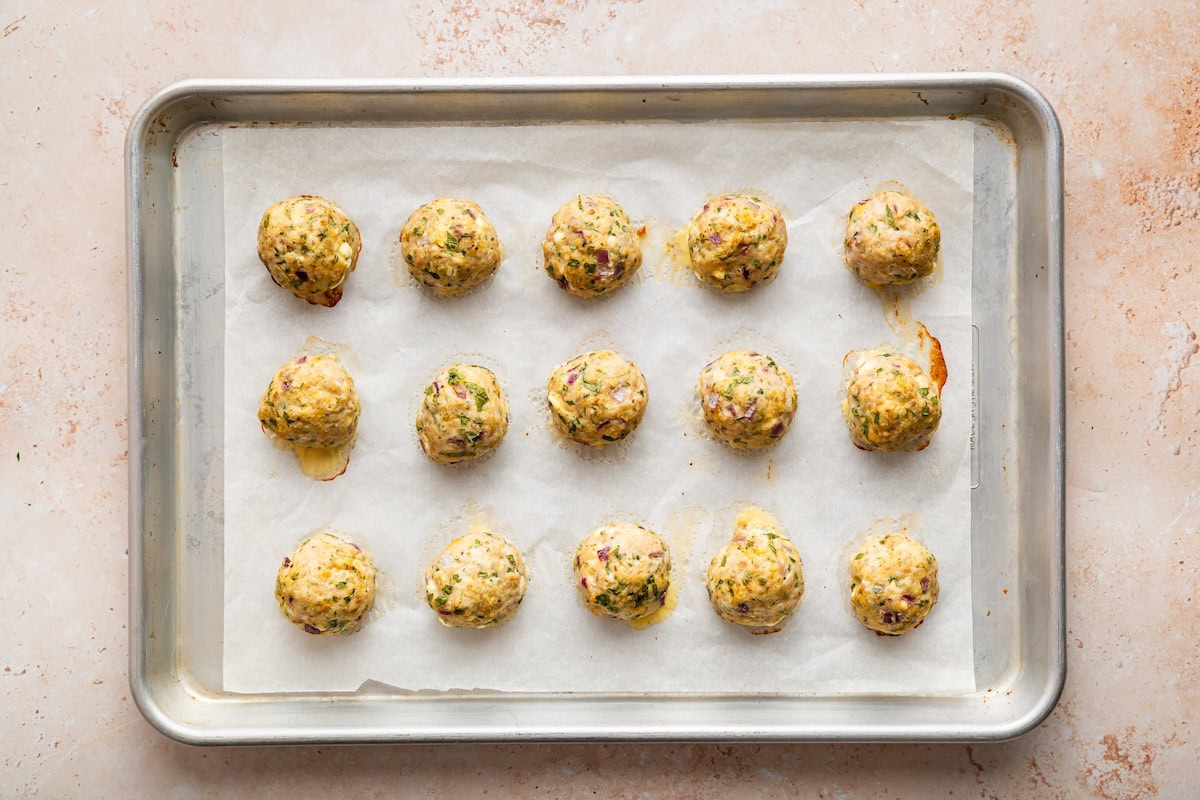 Fifteen Greek turkey meatballs on a baking tray after being baked in the oven.