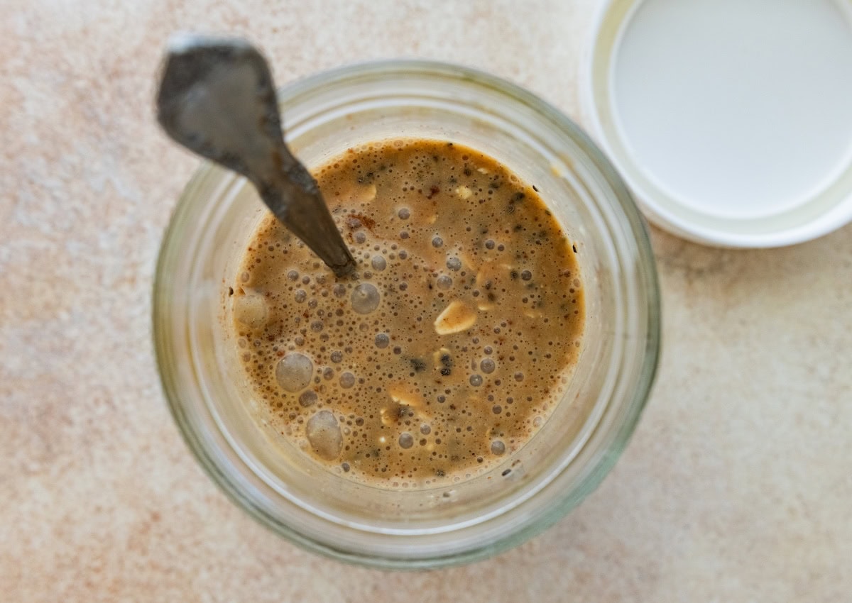 Mixing espresso with oats, chia seeds and protein powder in glass jar.