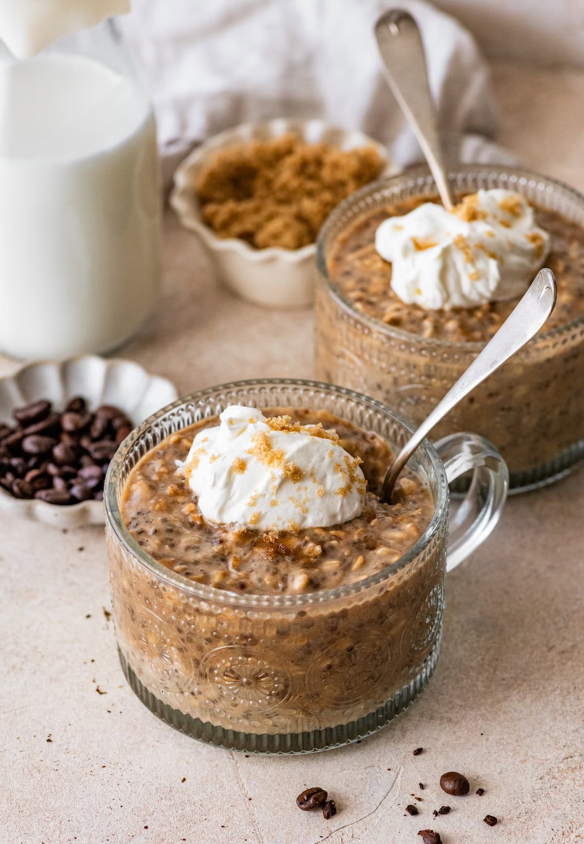 Brown sugar shaken espresso overnight oats topped with whipped cream in glass jars with spoons.