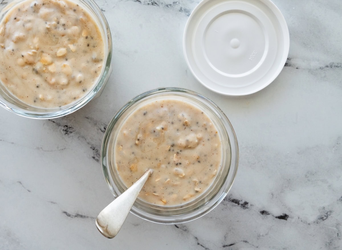 Two jars of coconut overnight oats stirred together in a glass jar with a spoon.