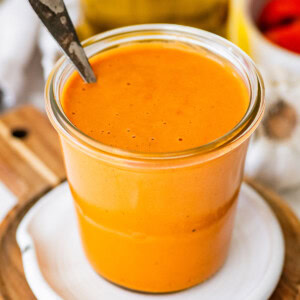 Spoon dipping into creamy roasted red pepper dressing showing thick, smooth consistency in jar.