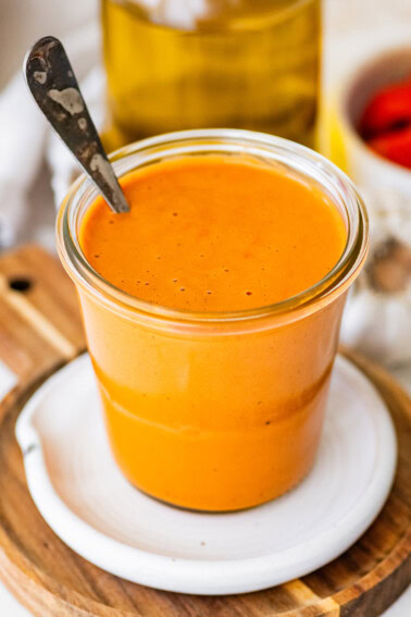 Spoon dipping into creamy roasted red pepper dressing showing thick, smooth consistency in jar.