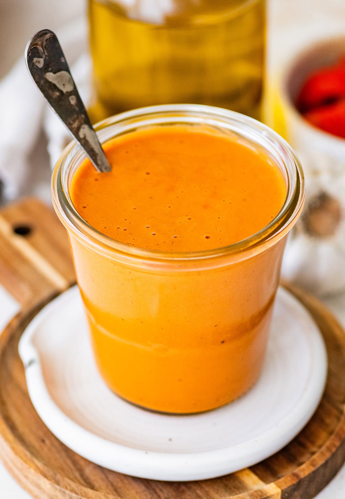 Spoon dipping into creamy roasted red pepper dressing showing thick, smooth consistency in jar.