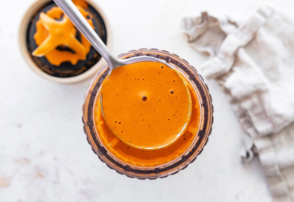 Creamy roasted red pepper dressing being spooned out from a blender.