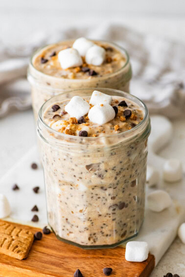 Two glass jars of s'mores overnight oats with marshmallows and chocolate chips.