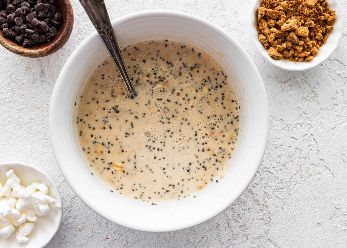 A large mixing bowl with milk, chia, and oats used for s'mores overnight oats.