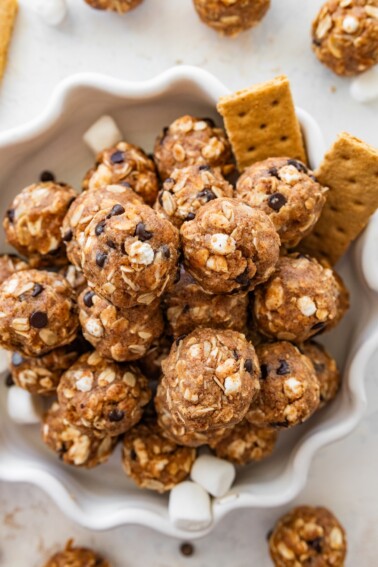 No-bake s’mores protein balls served on a decorative white plate alongside graham crackers and mini marshmallows.