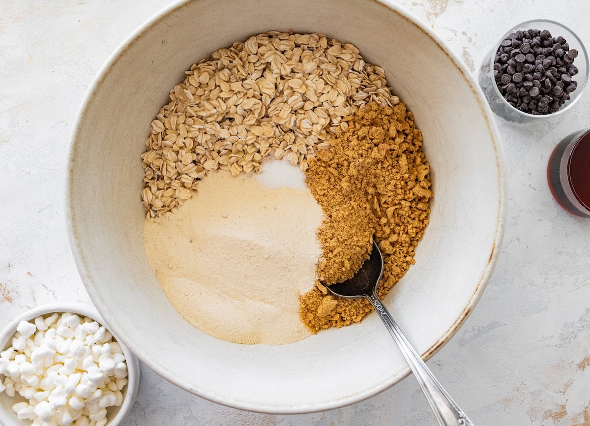 Oats, graham crackers and protein powder in a bowl for s’mores protein balls being mixed with a spoon.