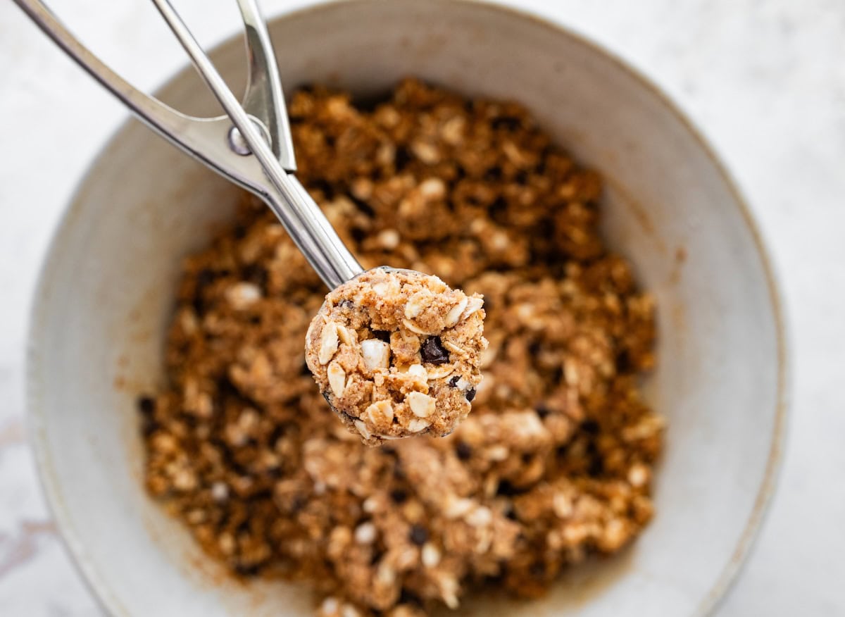 Scooping s’mores protein ball mixture with a cookie scoop from a mixing bowl.